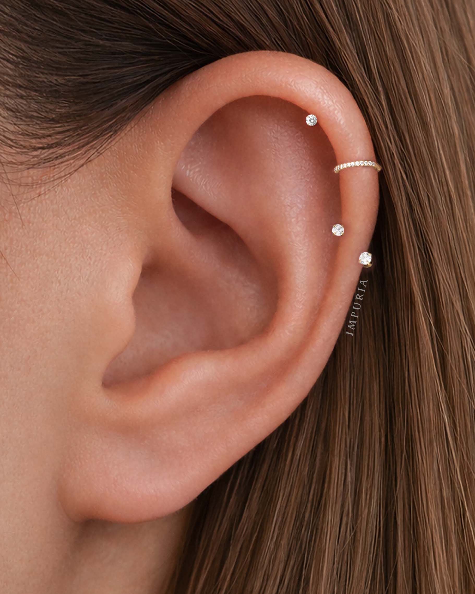 Close-up of helix on ear wearing three flat back stud earrings and a thin helix hoop, styled minimalist ear stack in gold