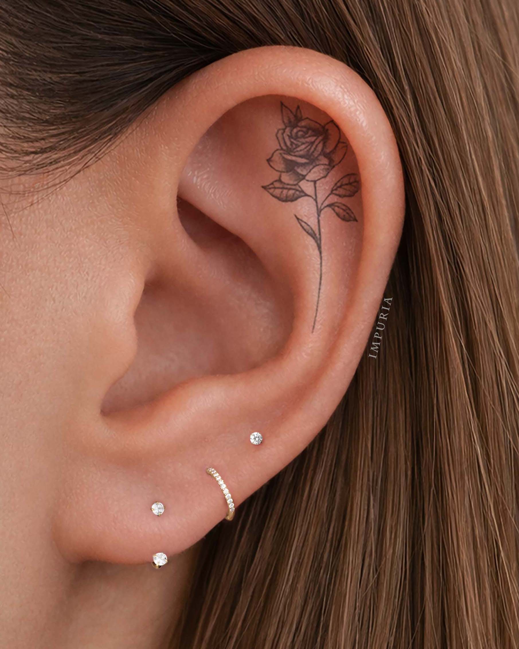 Close-up of helix on ear wearing three flat back stud earrings and a thin helix hoop, styled minimalist ear stack in gold