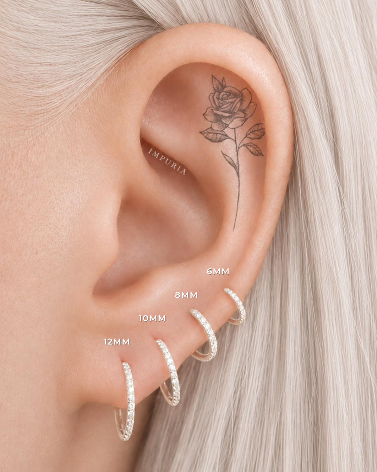 Close-up of a person's ear wearing four silver hoop earrings in different sizes (12MM, 10MM, 8MM, 6MM) with white text labels indicating the sizes. The person has platinum blonde hair and a rose tattoo on their ear cartilage.