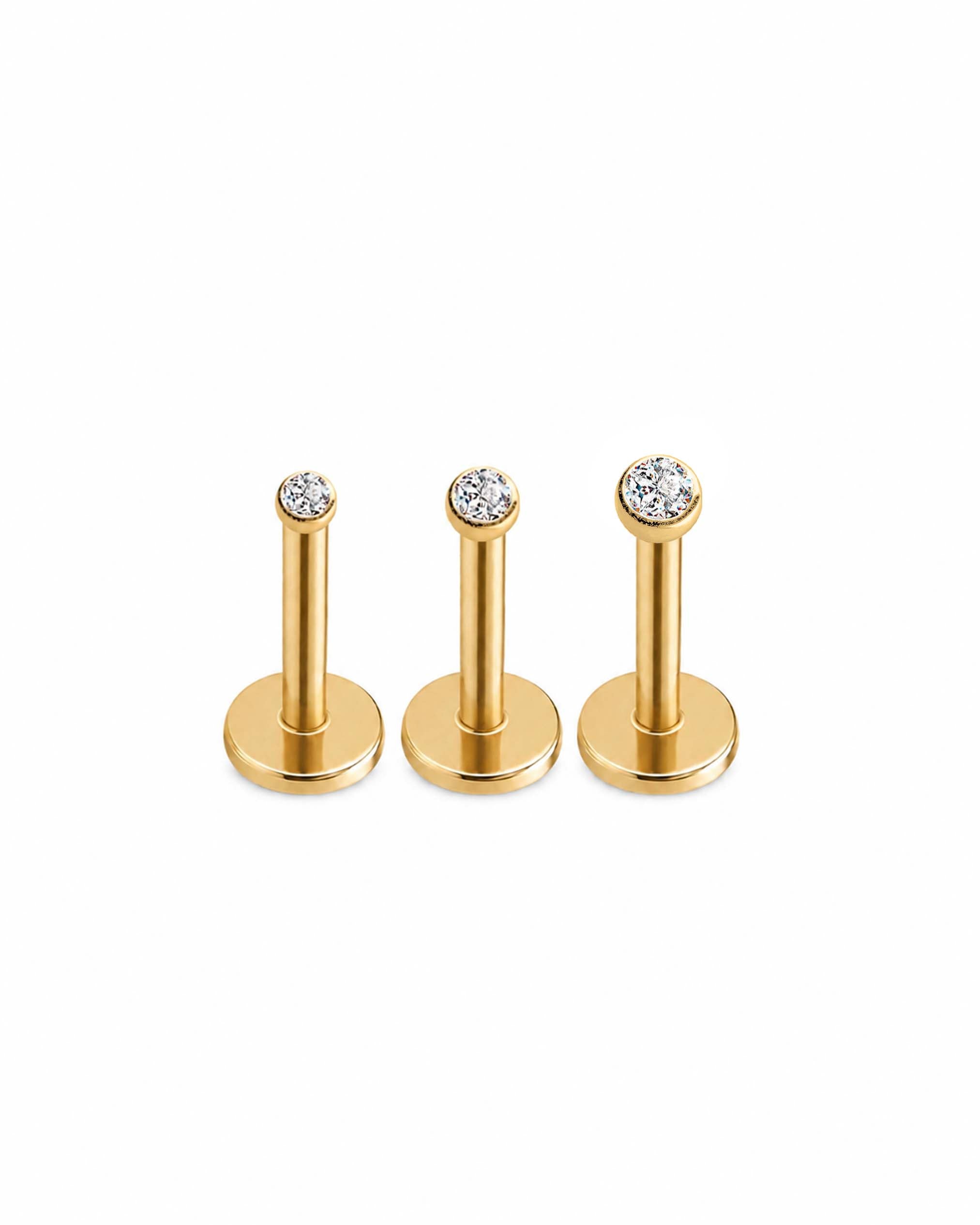 Three gold-tone flat-back labret piercings with round bezel-set clear gemstones, arranged in descending size order on a plain white background.