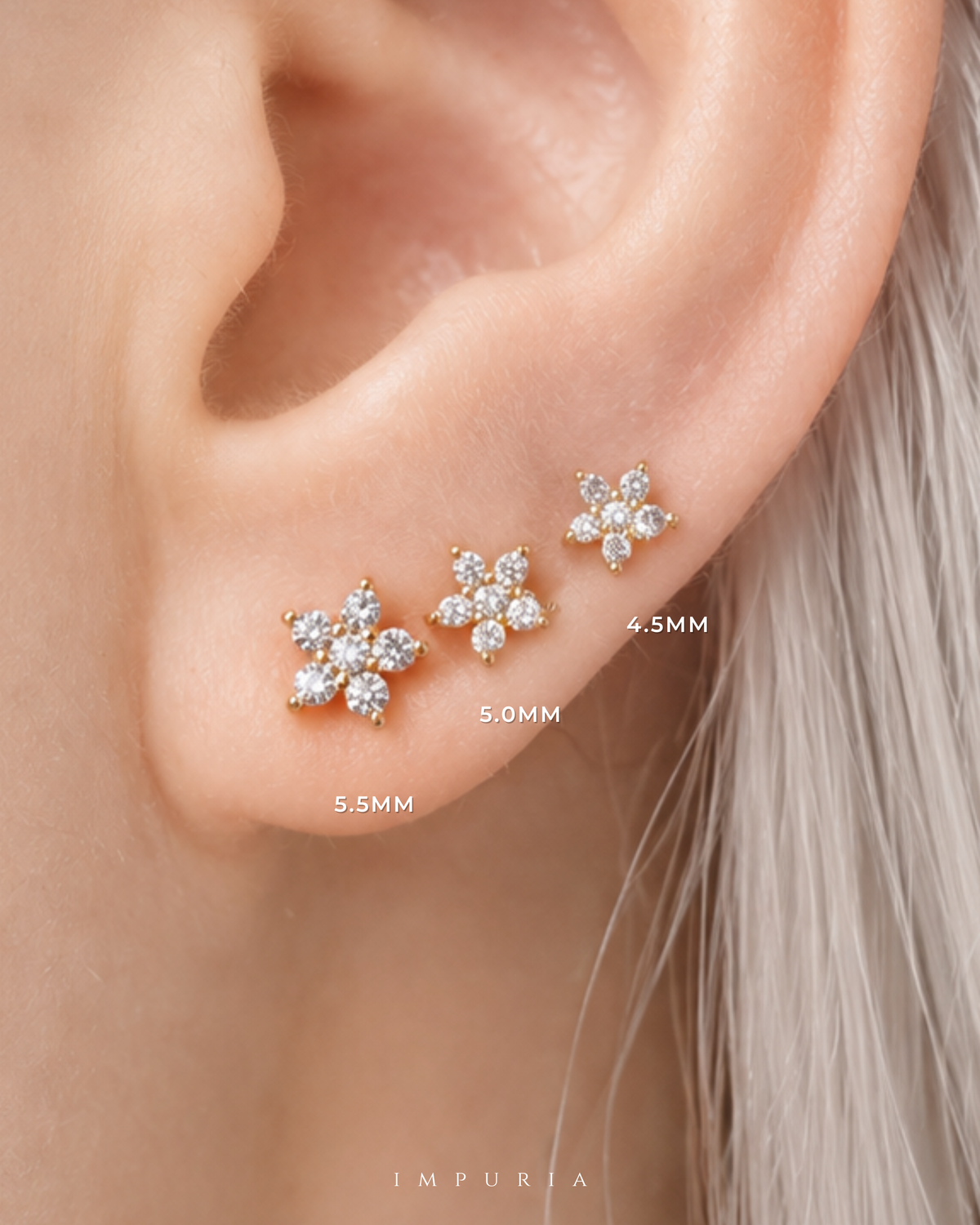 Close-up of a person's ear showing three gold flower-shaped stud earrings with clear stones in different sizes labeled 4.5MM, 5.