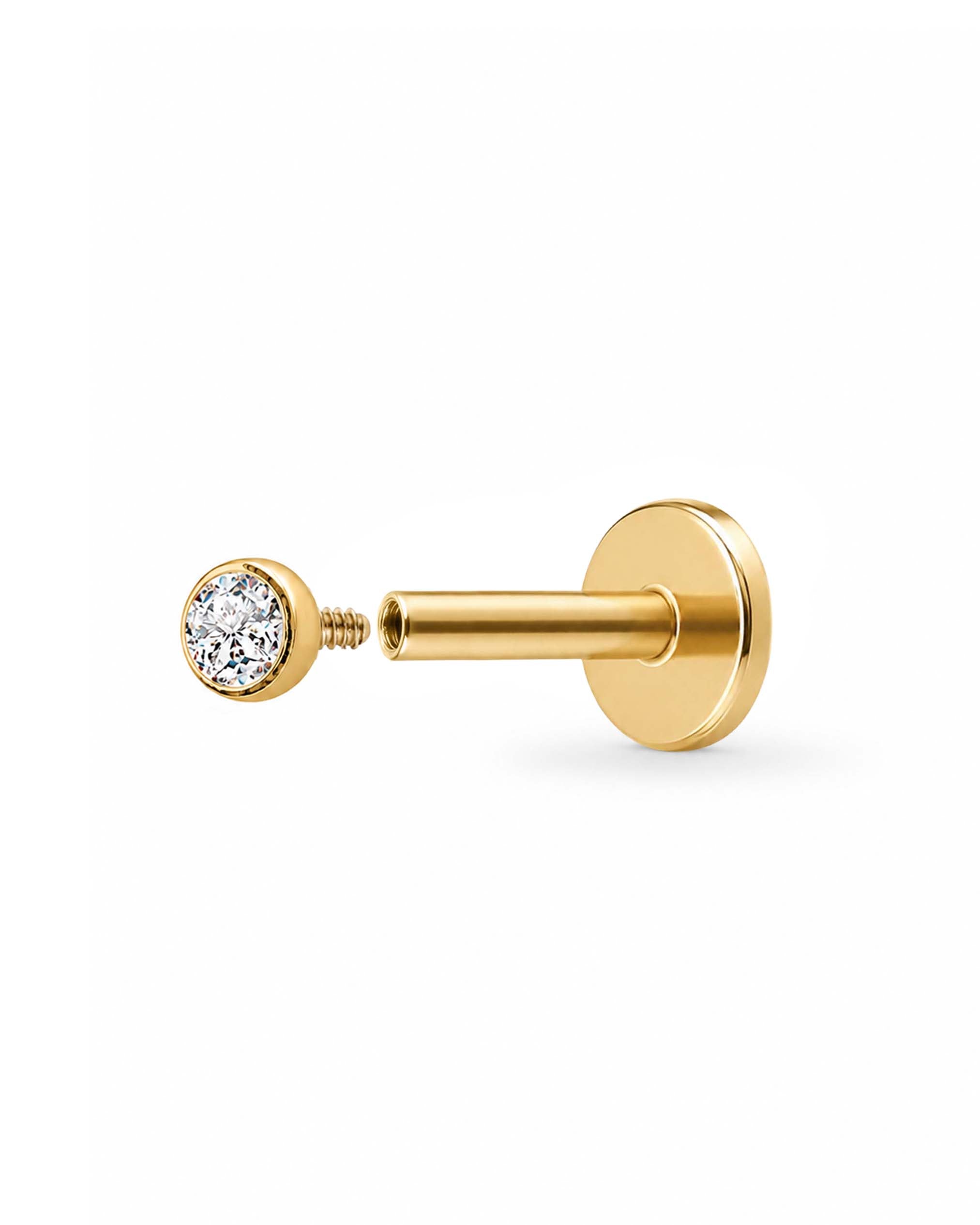 A gold-colored labret piercing stud with a round bezel-set clear gemstone on the post, shown against a plain white background.