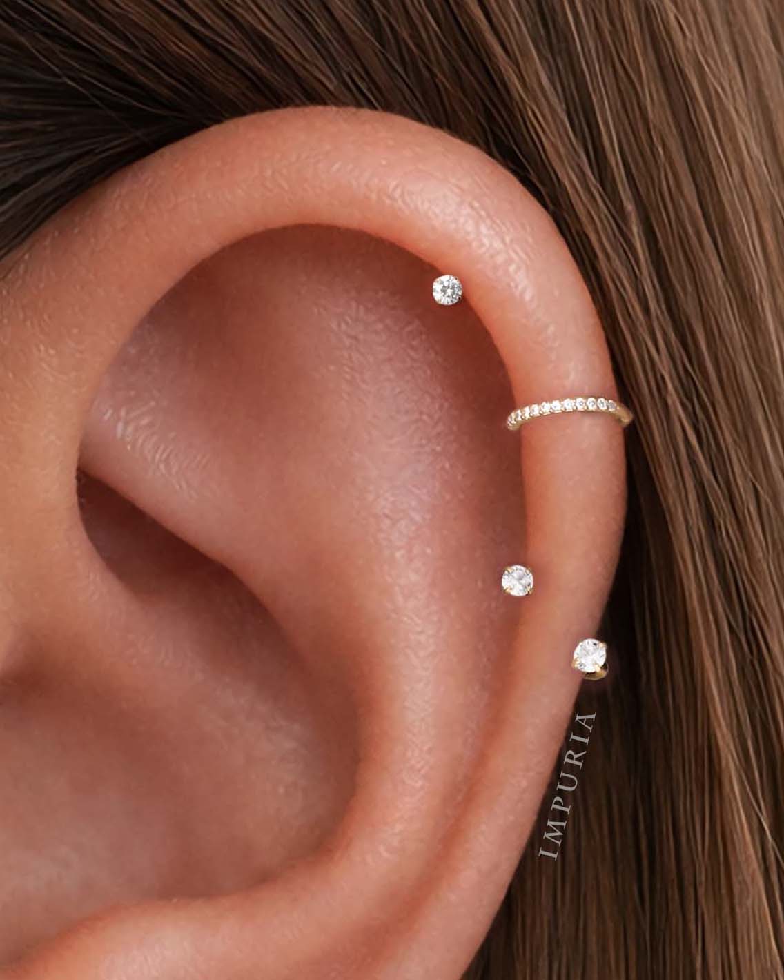 Close-up of helix on ear wearing three flat back stud earrings and a thin helix hoop, styled minimalist ear stack in gold