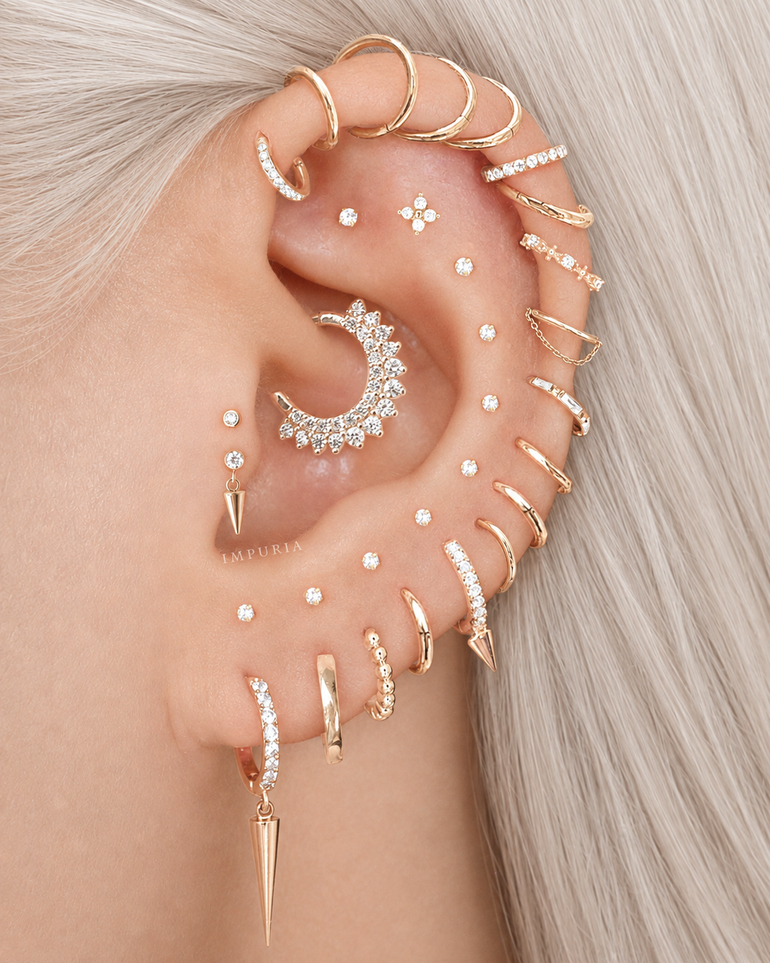 A close-up of a person's ear adorned with multiple rose gold and silver stud, hoop, and cartilage earrings, styled against light blonde hair ear stack inspo.