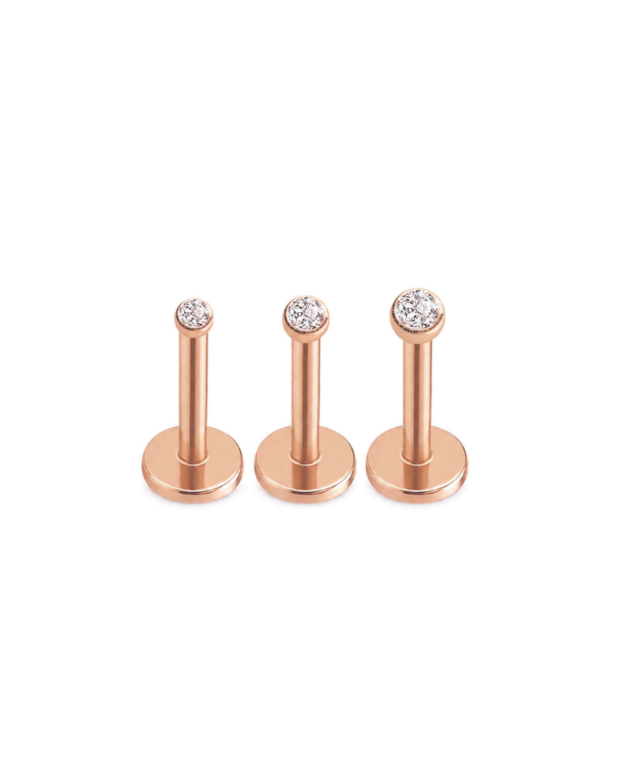 Three rose gold flat-back labret studs with clear gemstones, arranged in a row against a solid white background.