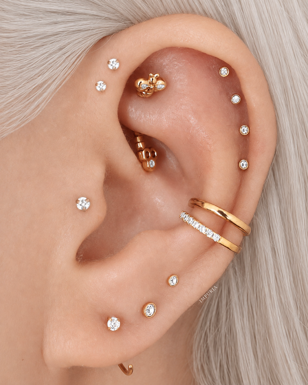 Close-up of a person's ear adorned with multiple gold and silver ear piercings and stud earrings, with light gray hair visible around the ear.